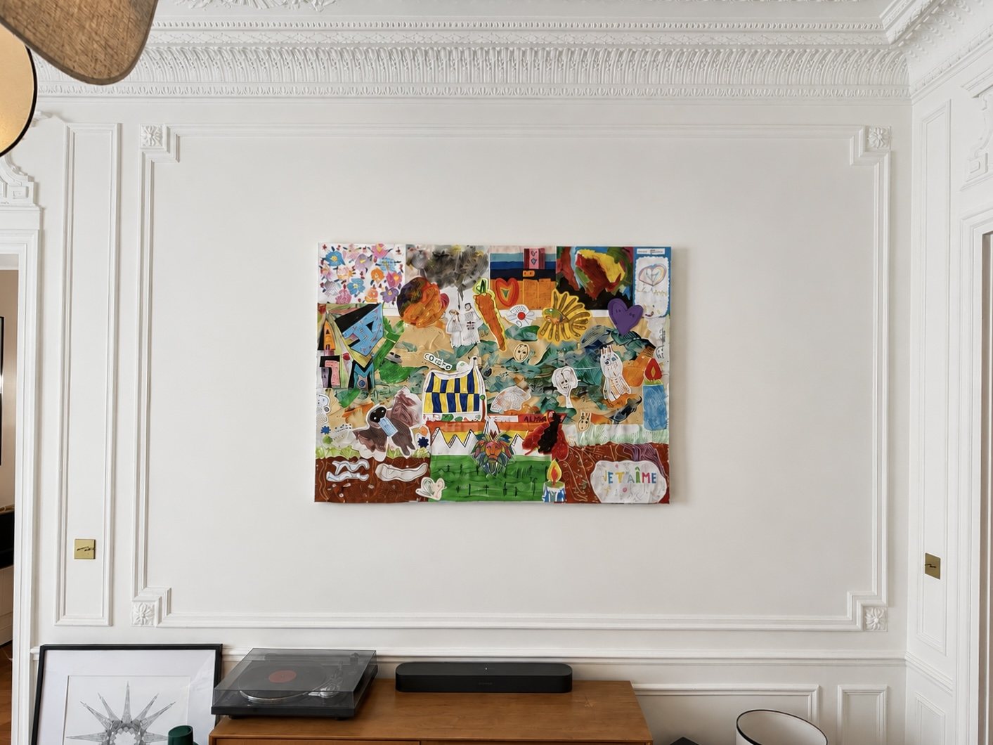 Un tableau composé de dessins d’enfants découpés et collés, accroché au mur d’un salon